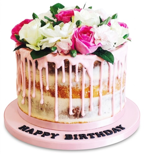 Round semi-naked cake with pink drip icing, topped with pink and white fresh flowers, on a pink cake board.