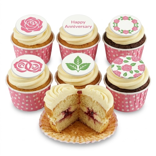 Vanilla and chocolate cupcakes with white frosting, pink polka dot wrappers, and various pink rose and green leaf anniversary toppers.