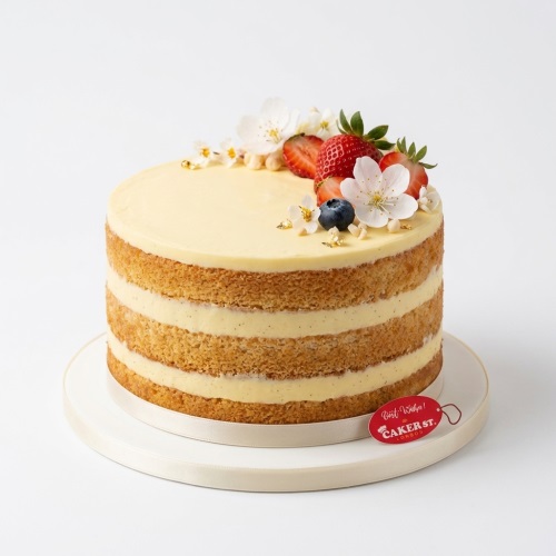 Three-layer naked cake with cream frosting, topped with white flowers, strawberries, blueberries, and gold flakes.