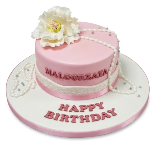 Pink round birthday cake with white sugar flower, pearl strands, and lace detail.