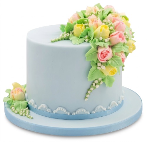 Light blue round birthday cake with pink and yellow piped flowers and green leaves.