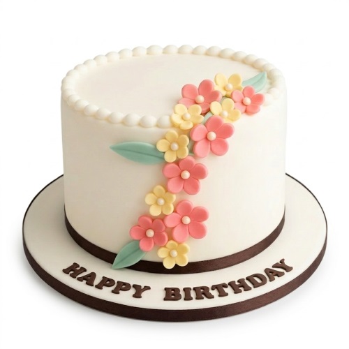 White round birthday cake decorated with pink and yellow sugar flowers, green leaves, and a 'Happy Birthday' message.