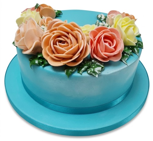 Round teal cake decorated with peach, pink, and yellow buttercream roses and green leaves, with a teal ribbon around the base.