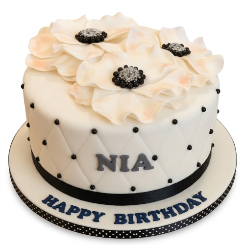 Round white birthday cake with cream flowers, black beaded centres, quilted sides, and a black polka dot board.