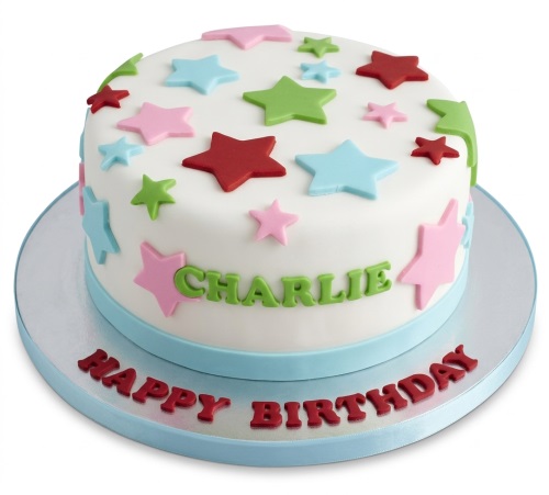 White round birthday cake decorated with colourful red, pink, blue, and green stars, with a personalised name on the side.