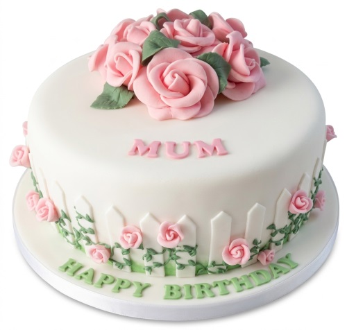 Round white fondant cake decorated with pink sugar roses, green leaves, and a white picket fence design with green vines and small pink roses.