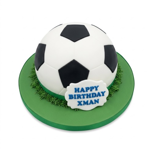 Spherical football birthday cake with black and white panels on a green grass-effect base and a custom message plaque.
