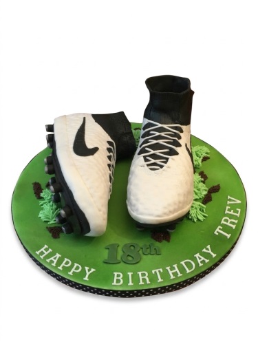 Round green cake with 3D white and black football boots, custom age, and personalised message.