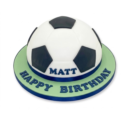 3D football birthday cake with white and black panels on a green base with a personalised message.