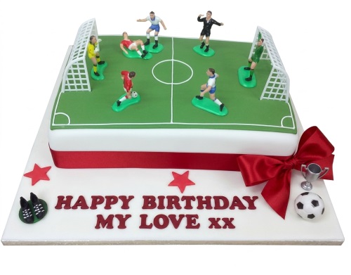 Square football pitch cake with player figurines, goals, football, trophy, and red ribbon.