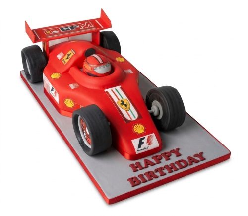 Red Ferrari Formula 1 racing car 3D sculpted birthday cake with 'Happy Birthday' message on the base.