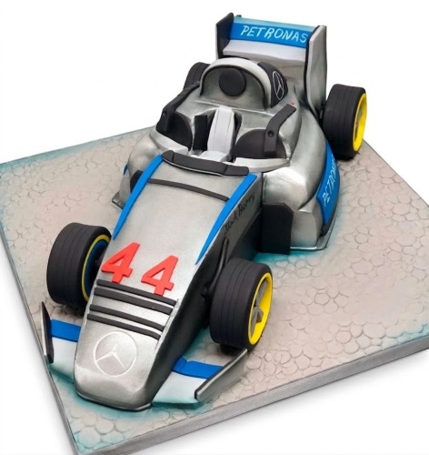 Silver Formula 1 racing car cake with blue and black details, yellow wheels, and number 44 on a textured cake board.