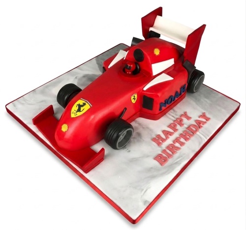 3D red Ferrari racing car birthday cake on a grey board with a custom name and message.