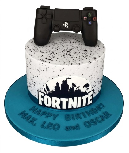 Round white Fortnite themed birthday cake with a black gaming controller topper and black speckle design.