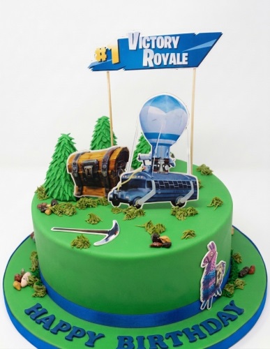 Round green Fortnite themed birthday cake with Victory Royale topper, Battle Bus, treasure chest, pickaxe, and Llama decorations.