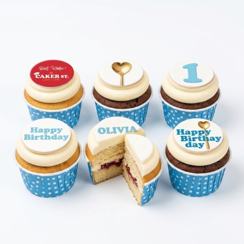 Vanilla and chocolate cupcakes with white icing, blue polka dot wrappers, and custom age/name toppers.
