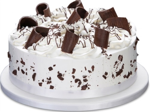 Round white cake with whipped cream, chocolate curls, chocolate drizzle, and chocolate flakes on a white cake board.