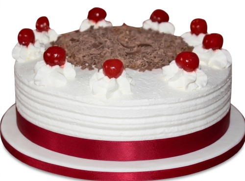 Round Black Forest style cake with white cream, chocolate shavings, and red cherries, with a red ribbon.