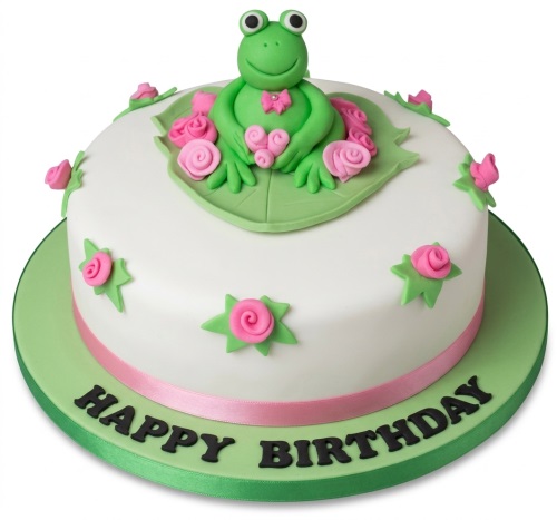 Round white fondant cake with a green frog on a lily pad, pink roses, and a pink ribbon. Features a 'Happy Birthday' message.