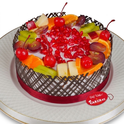 Round fresh fruit cake with cherries, pomegranate, kiwi, orange, grapes, and chocolate lattice.