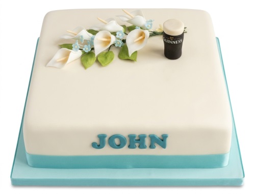 Square cream fondant cake with a miniature Guinness pint topper, white calla lilies, and blue accent flowers.