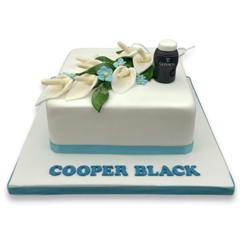 White square cake with white calla lilies, blue flowers, green leaves, and a miniature Guinness bottle.