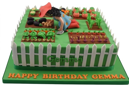 Rectangular green gardening theme birthday cake with fondant vegetables, a female gardener figure, and a white picket fence.