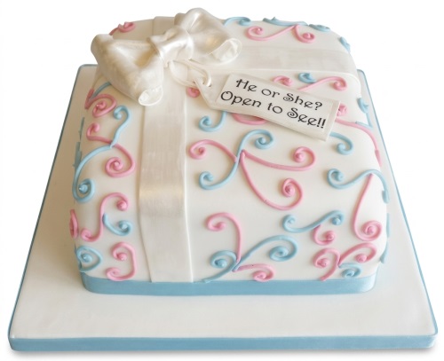 White gift box shaped gender reveal cake with pink and blue swirls, white bow, and 'He or She? Open to See!!' tag.