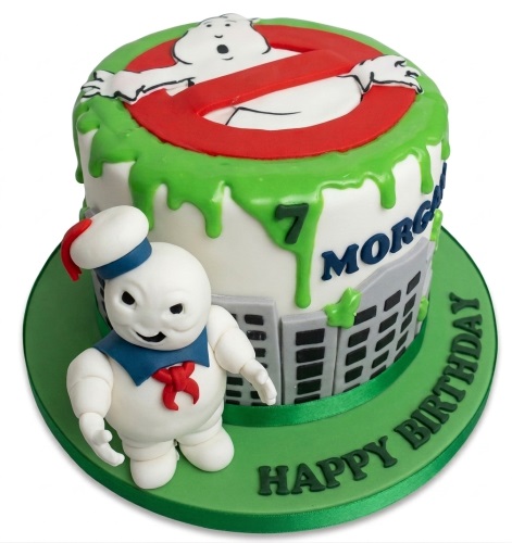 Ghostbusters themed birthday cake with Stay Puft Marshmallow Man figure, green slime drip, and city buildings.