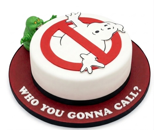 Round white Ghostbusters themed birthday cake with red no-ghost logo, green Slimer character, and "WHO YOU GONNA CALL?" on the board.