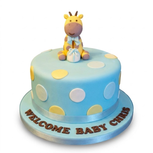 Round blue baby shower cake with yellow and white polka dots, topped with a yellow fondant giraffe holding a small gift, and a personalised message on the board.