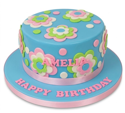 Round blue birthday cake with pink, green, and white layered flowers and polka dots. Features a pink ribbon and personalised name.