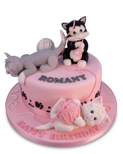 Pink round birthday cake with three fondant cats and pink yarn decorations.