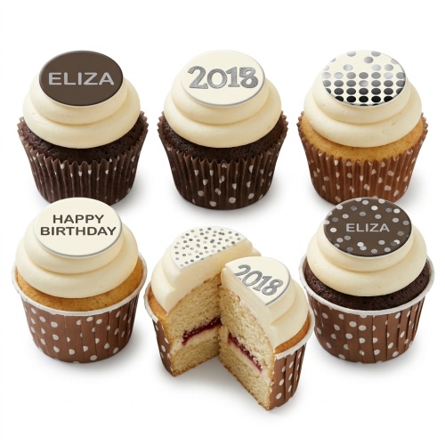 Assortment of classic cupcakes with cream frosting and customisable polka dot, name, and year toppers in brown and white cases.