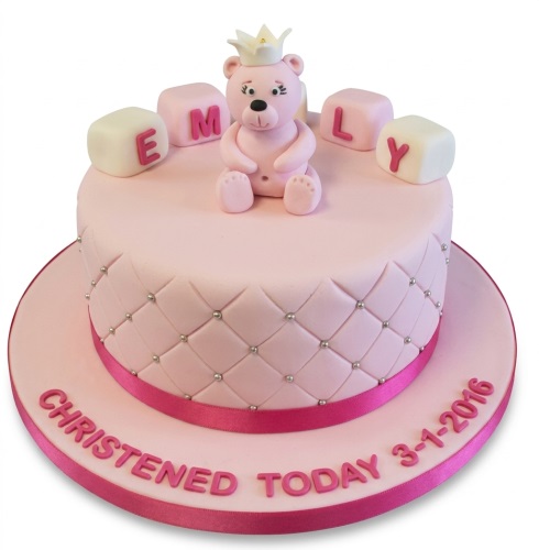 Pink single-tier cake with a teddy bear wearing a crown, letter blocks, quilted pattern, and a pink ribbon.