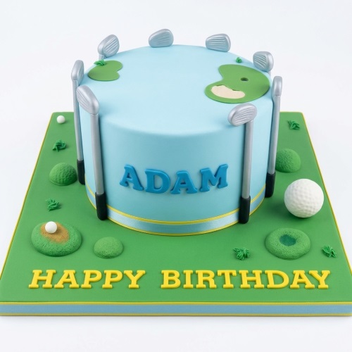 Round light blue golf theme birthday cake with edible golf clubs, golf balls, and green putting areas on a green cake board.