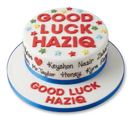 Two-tier white good luck cake with red text, colourful stars, and blue ribbon.
