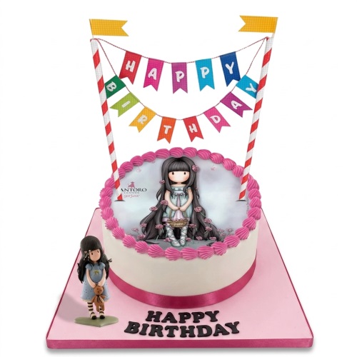 Round white birthday cake with Gorjuss doll edible image, pink piping, and 'Happy Birthday' banner.