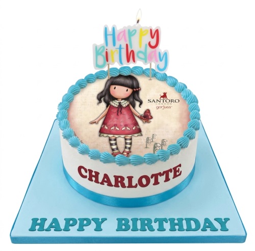 White round Gorjuss doll birthday cake with blue trim and "Happy Birthday" candle topper.
