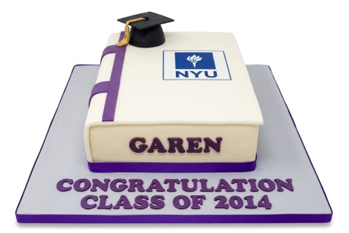 White book-shaped graduation cake with purple ribbon, black graduation cap, and university logo.