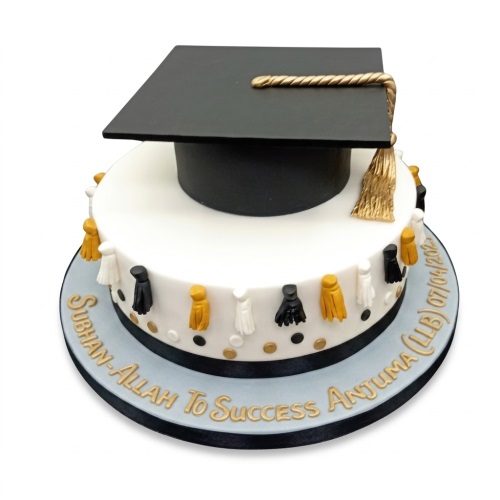 White single-tier graduation cake with a black cap, gold tassel, and black, white, gold tassels around the side.