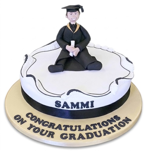 Round white graduation cake with a graduate figurine, black ribbon, and custom message on the board.