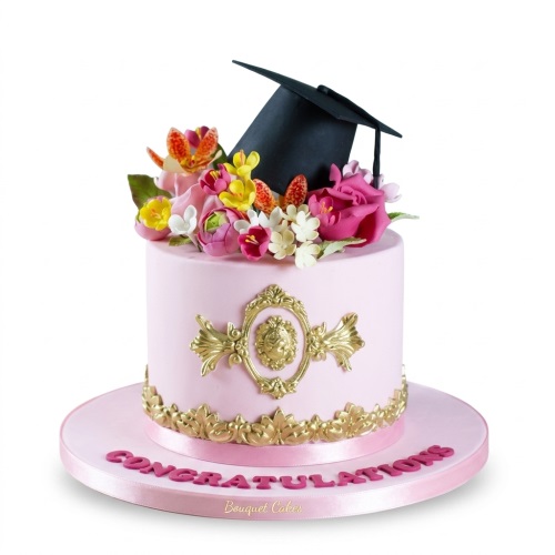 Elegant pink graduation cake with a black cap, colourful sugar flowers, and gold ornate decorations, with 'CONGRATULATIONS' on the board.