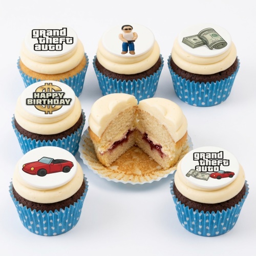 Grand Theft Auto themed cupcakes with white frosting, blue polka dot wrappers, and edible toppers featuring GTA logo, character, money, and a red car, plus a 'Happy Birthday' message.