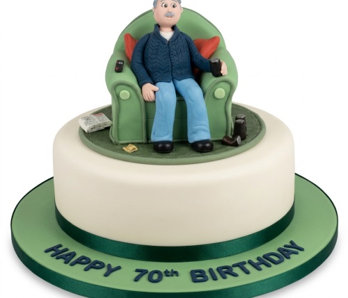 Round white cake with a figurine of a senior man relaxing in a green armchair with a newspaper and remote.