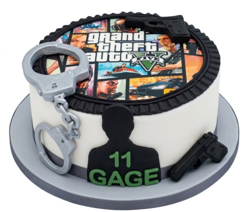 Round white Grand Theft Auto V themed birthday cake with edible game art, handcuffs, gun, and custom age and name.