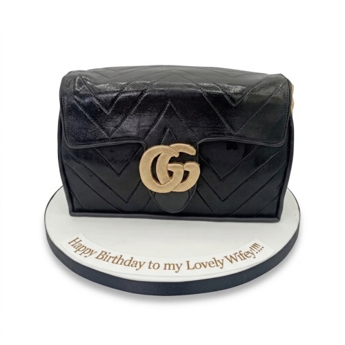 Black Gucci handbag shaped birthday cake with gold logo and custom message on board.