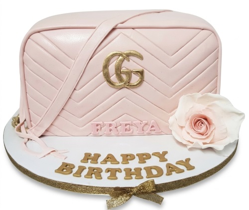 Pink quilted handbag cake with gold GG logo, shoulder strap, and a light pink rose.