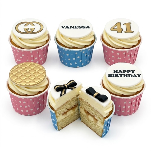 Vanilla cupcakes with white frosting, gold designer-style logo, quilted pattern, black bows, custom name and age toppers.