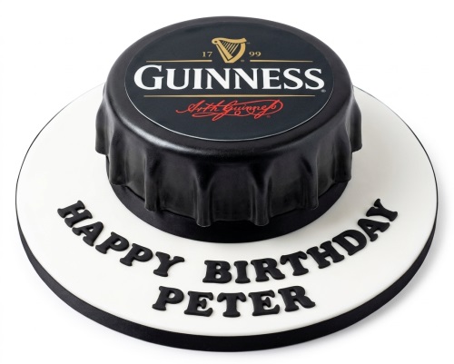 Round white cake board with a black Guinness bottle cap shaped cake on top, with 'Happy Birthday' and a custom name written on the board.